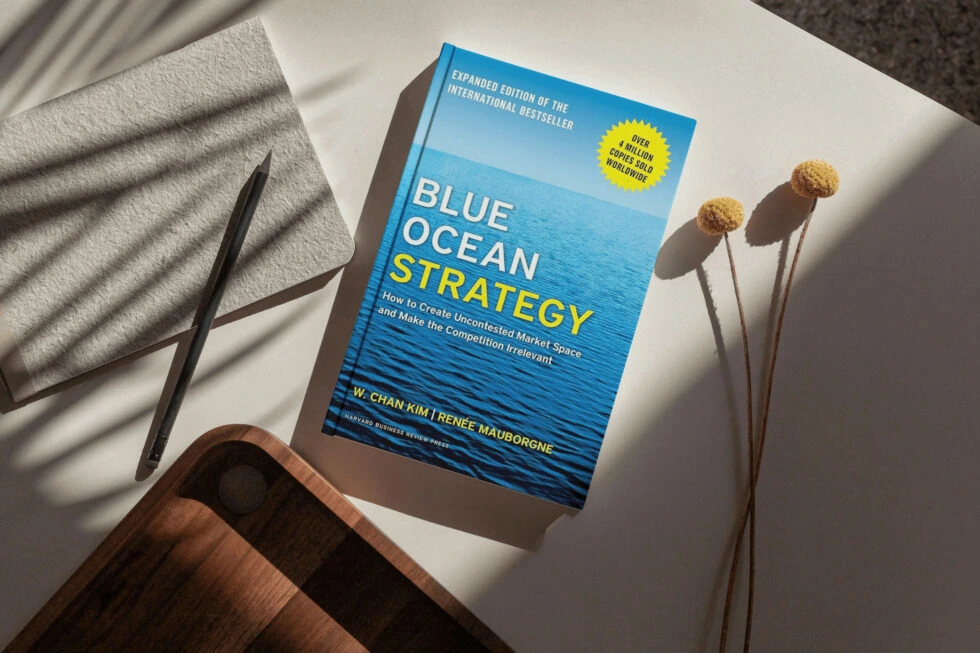 An expanded edition of the international bestseller "blue ocean strategy" by w. Chan kim and renee mauborgne, surrounded by a pen, dried flowers, and a cozy blanket, inviting readers to explore unconventional marketing strategies.