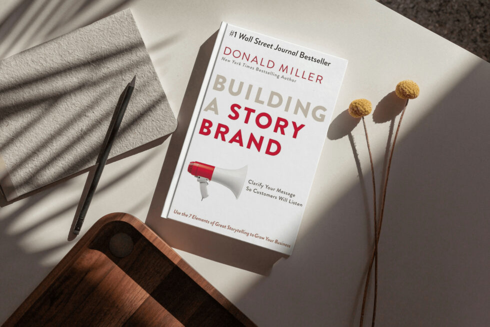 A book titled "building a story brand" by donald miller, a #1 wall street journal bestseller, lying on a table with a pen and dried flower stems, showcasing the importance of storytelling in branding.