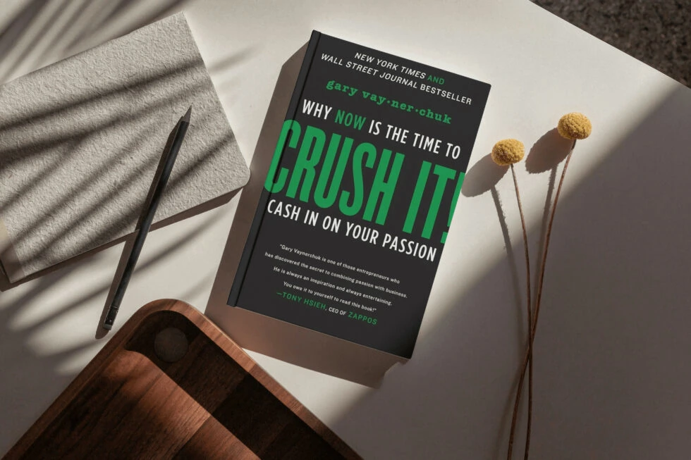 A book titled "why now is the time to crush it: cash in on your passion" by gary vaynerchuk, along with a pen, flowers, and a wooden surface.