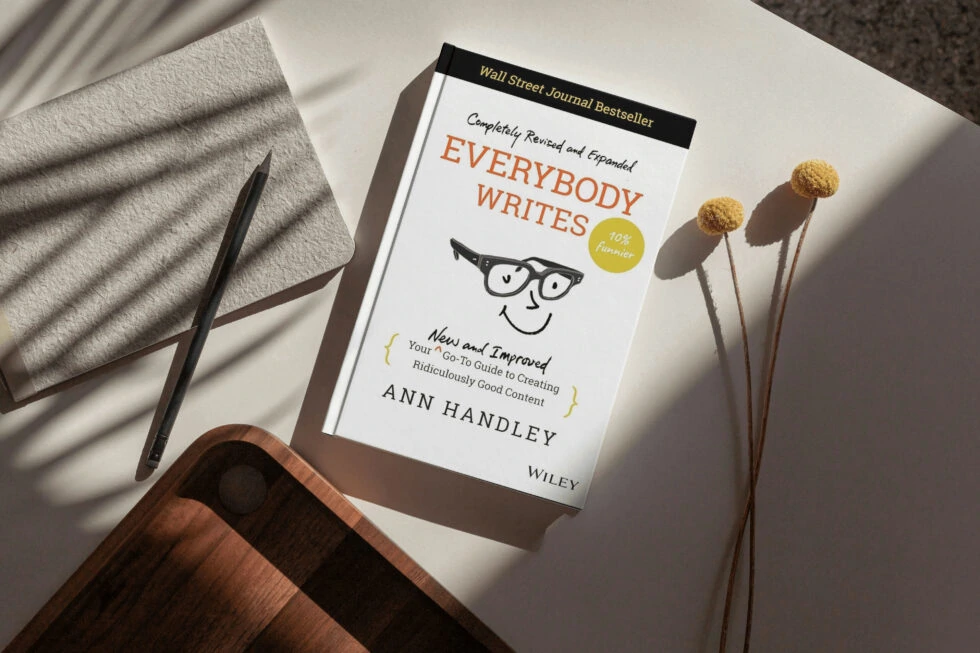 A copy of the wall street journal bestseller "everybody writes" by ann handley, a practical guide to creating compelling content, nestled amongst a pen, dried flowers, and a cozy blanket