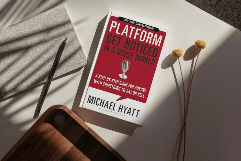 A book titled "platform: get noticed in a noisy world" by michael hyatt, along with a pen, dried flowers, and a wooden surface.